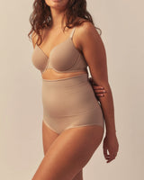 Woman wearing high-waisted sculpting shorts in a nude shade, providing light to medium support for a smooth, contoured fit. The seamless design enhances comfort and shaping.