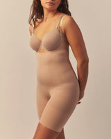  Woman wearing a black-colored sculpting bodysuit with medium to strong support, featuring a seamless design for targeted shaping, tummy control, and a smooth, contoured fit.